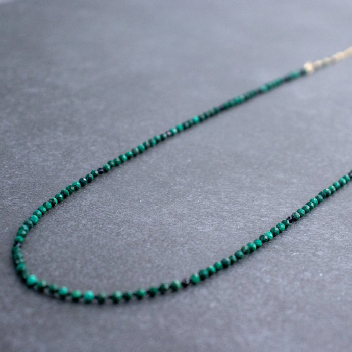 A vibrant green malachite bead necklace with black spinel accents, hand-knotted in a symmetrical pattern, delicately wire wrapped with a 14k gold filled satellite chain.